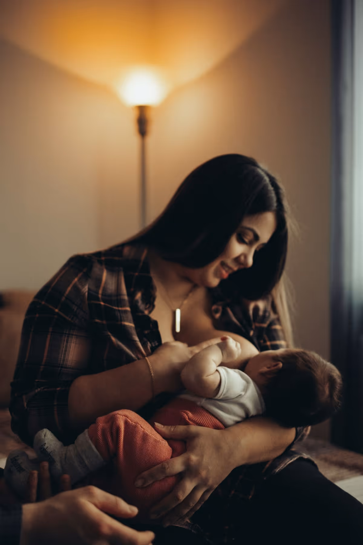 A mother cradling and feeding her baby in warm lamplight